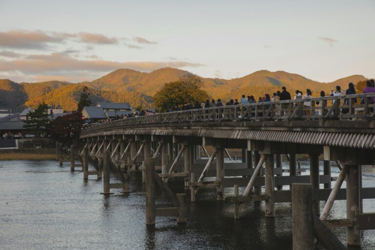 Anonymous people walking on bridge over river in ancient town at sundown